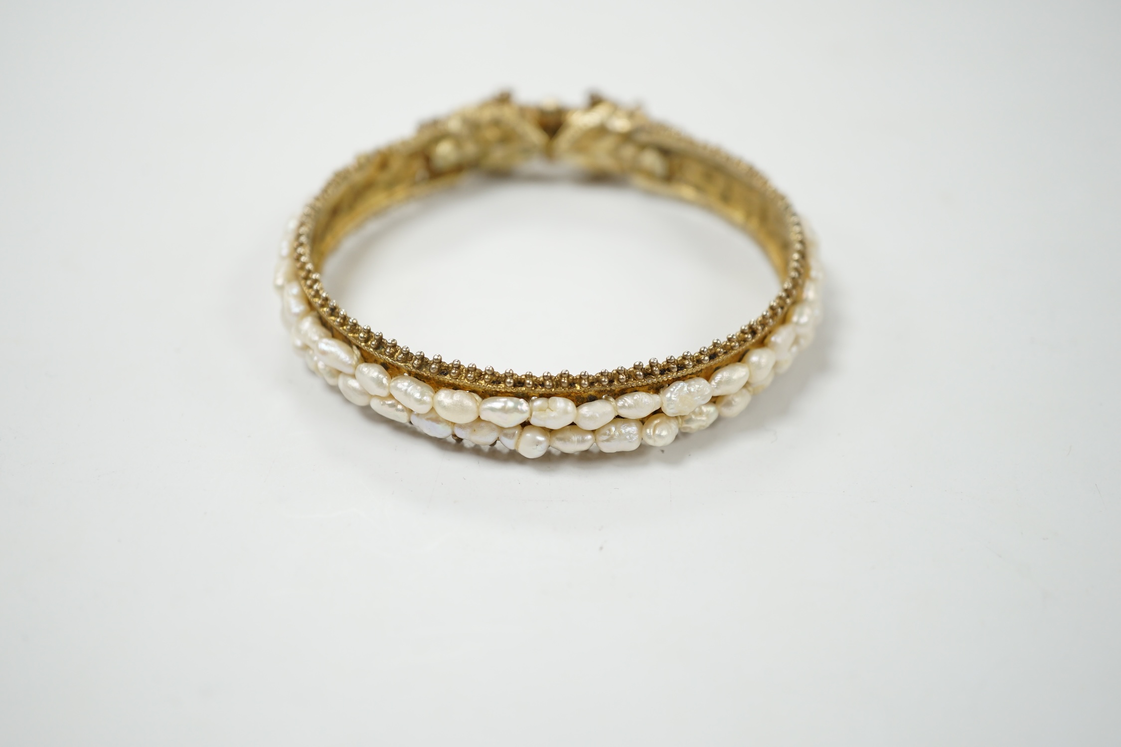A Chinese? gilt white metal and freshwater pearl cluster set hinged bangle, with red stone eyes. Condition - fair